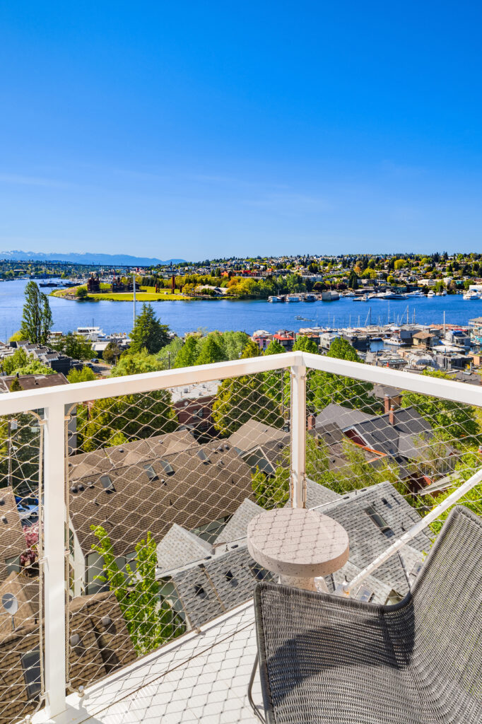 Balcony railing with safety netting overlooks a lake town with boats and houses under a clear blue sky.