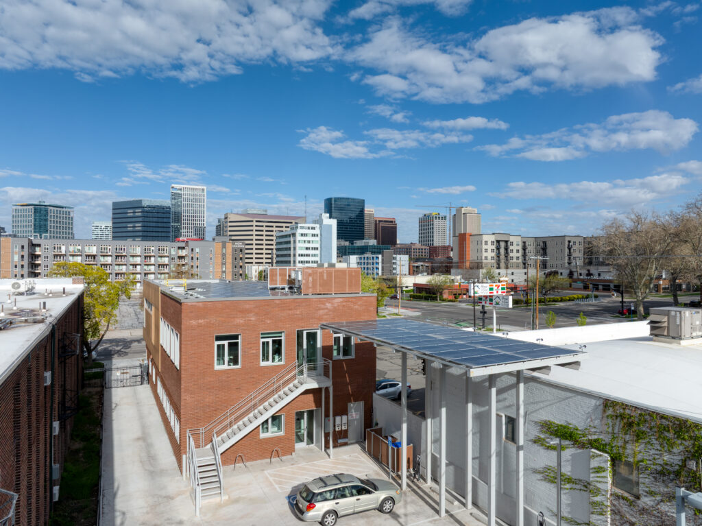 default - Living Future Rooftop view of brick buildings and a parking area with the city skyline in the distance under a blue sky with clouds: urban, daytime scene.