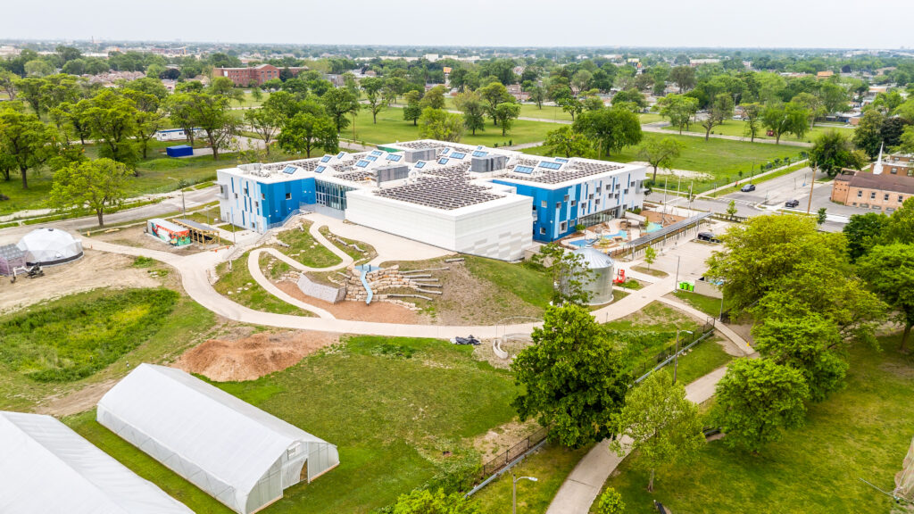 default - Living Future Aerial view of a modern blue-and-white campus building with solar panels on the roof, surrounded by green park.