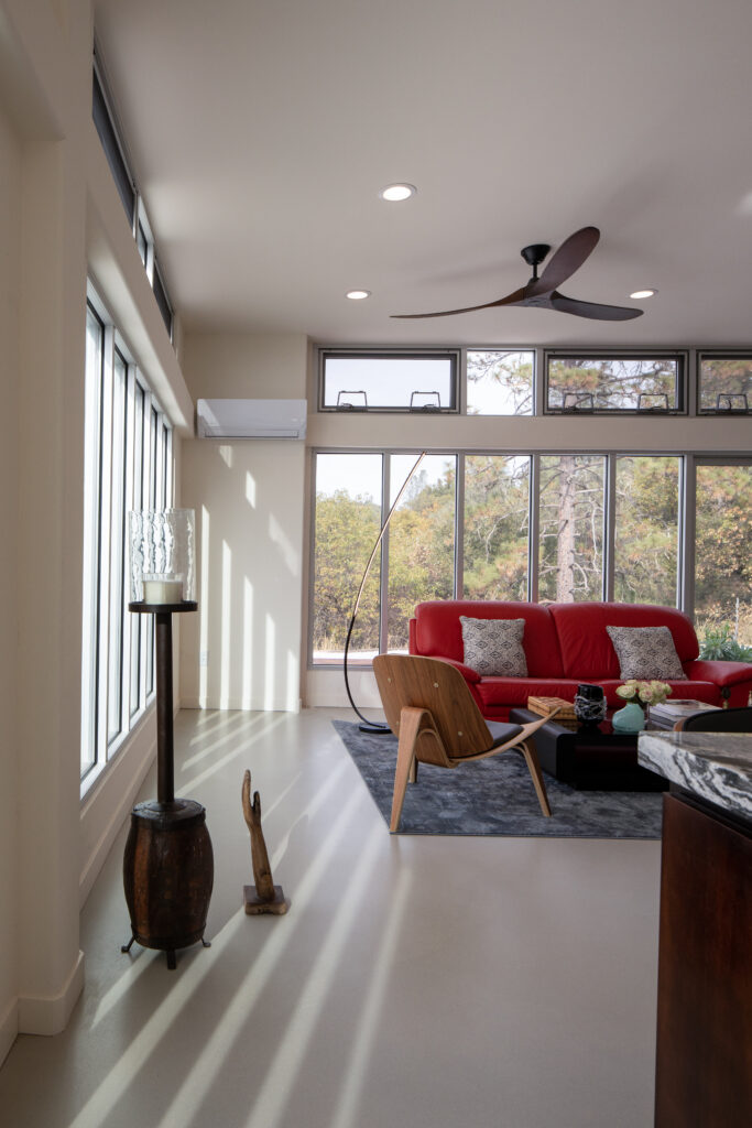 QuiteOak--23 - Living Future Bright living room with large windows, a red sofa, and modern seating under a ceiling fan and recessed lights.